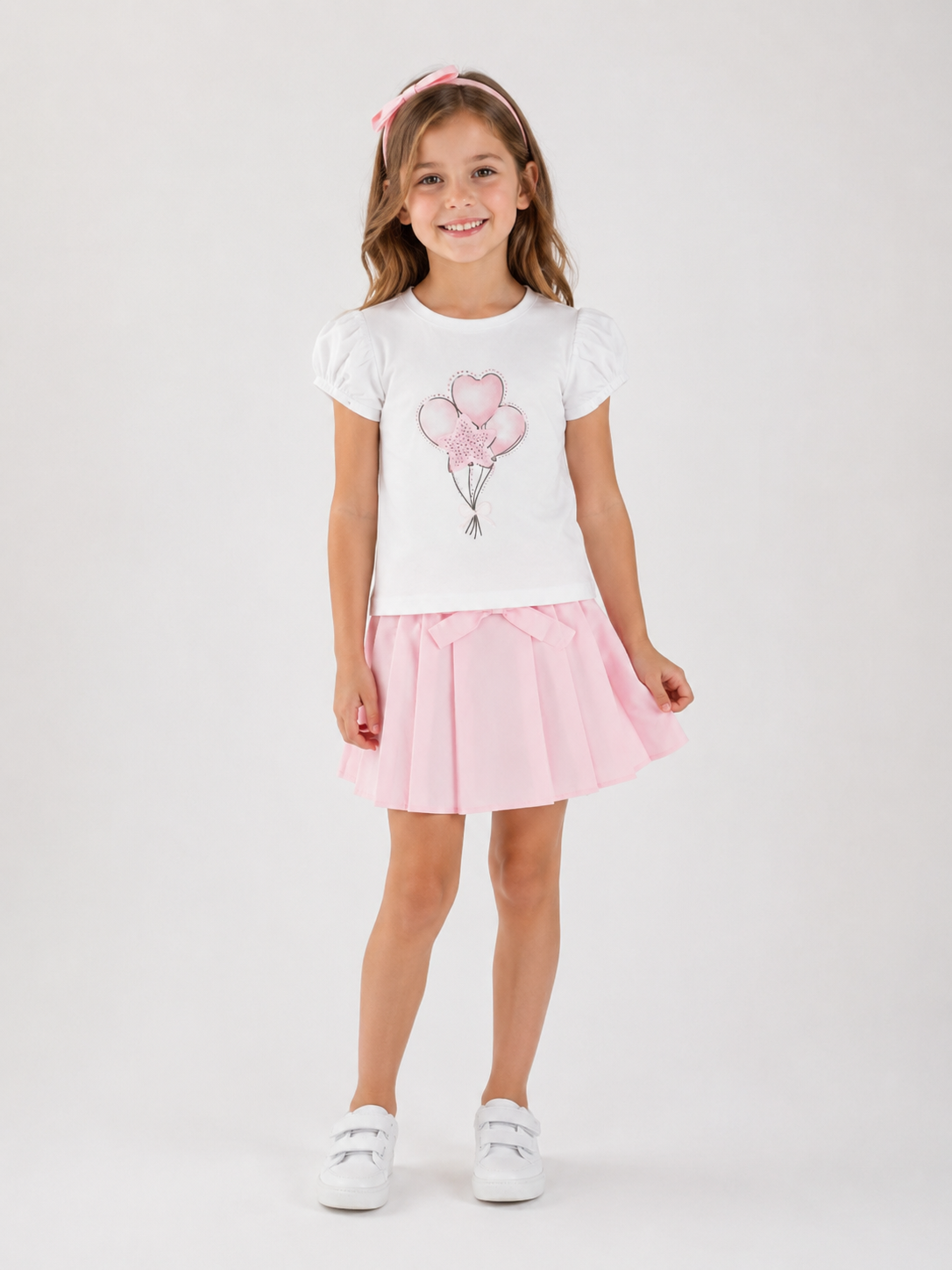 Meisje van 6 jaar draagt een witte iDO T-shirt met roze hartjesballonnen en een lichtroze plooirok