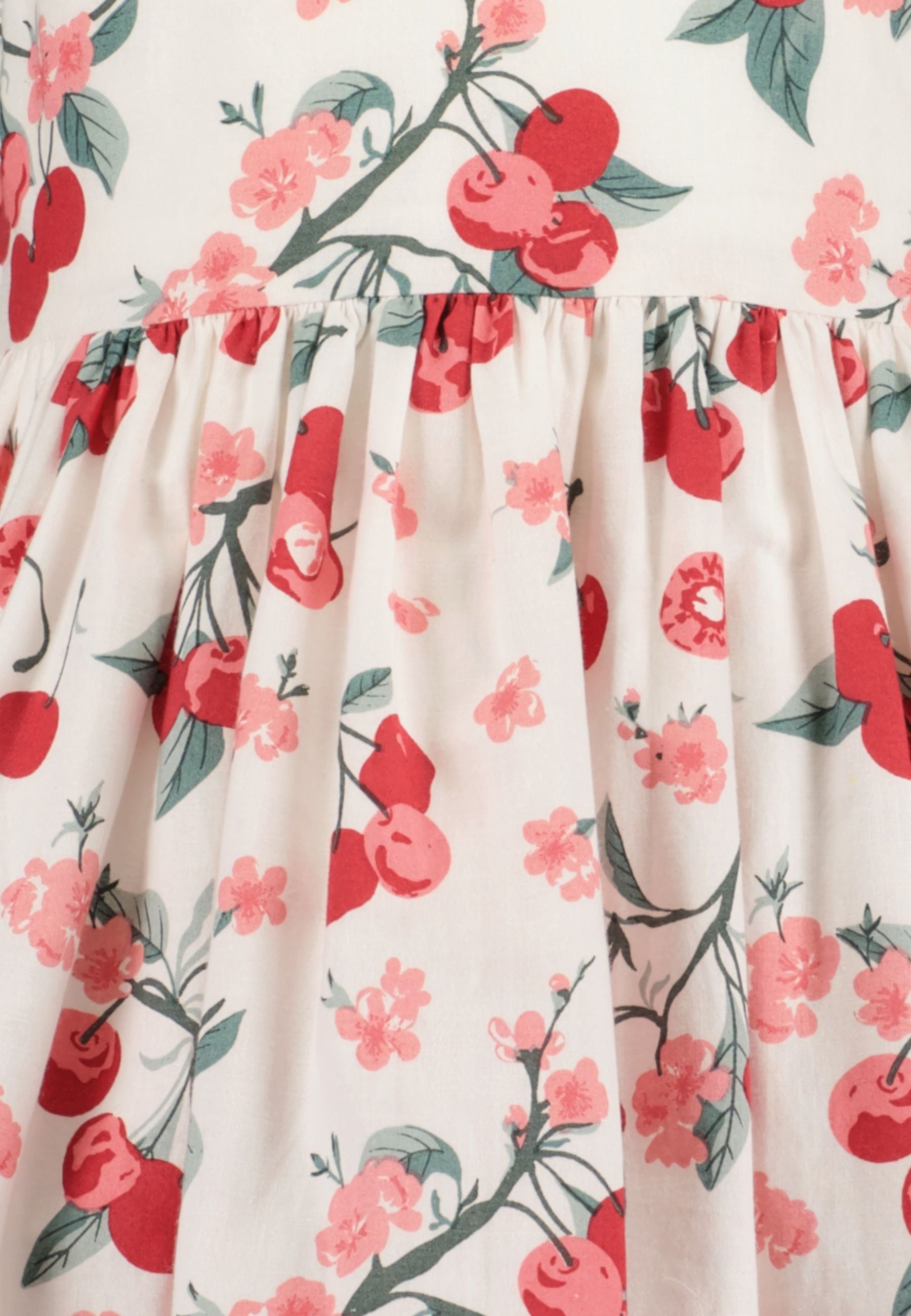 Lachend meisje draagt witte zomerjurk met kersen en bloesemprint en ruche vlindermouwtjes van Blue Seven – Elisa Kids Boutique